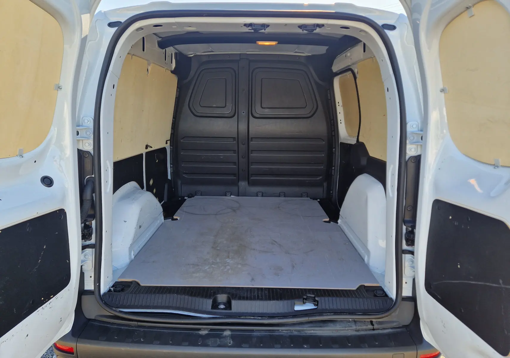 Vue arrière ouverte du Renault Kangoo blanc 2024, montrant l'espace de chargement vide avec parois en bois clair.