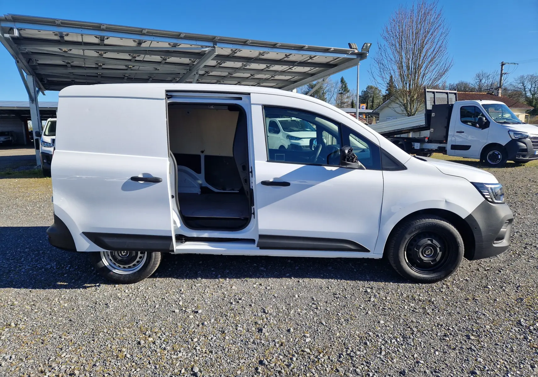 Vue de profil côté droit d’un Renault Kangoo blanc 2024 avec porte coulissante ouverte, montrant l’intérieur vide du van.