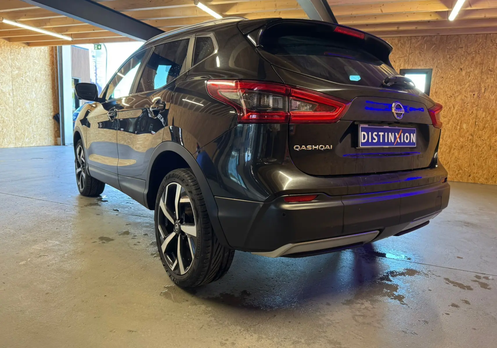 Vue 3/4 arrière droite d'un Nissan Qashqai noir 2017 avec jantes alu et barres de toit, stationné en intérieur.