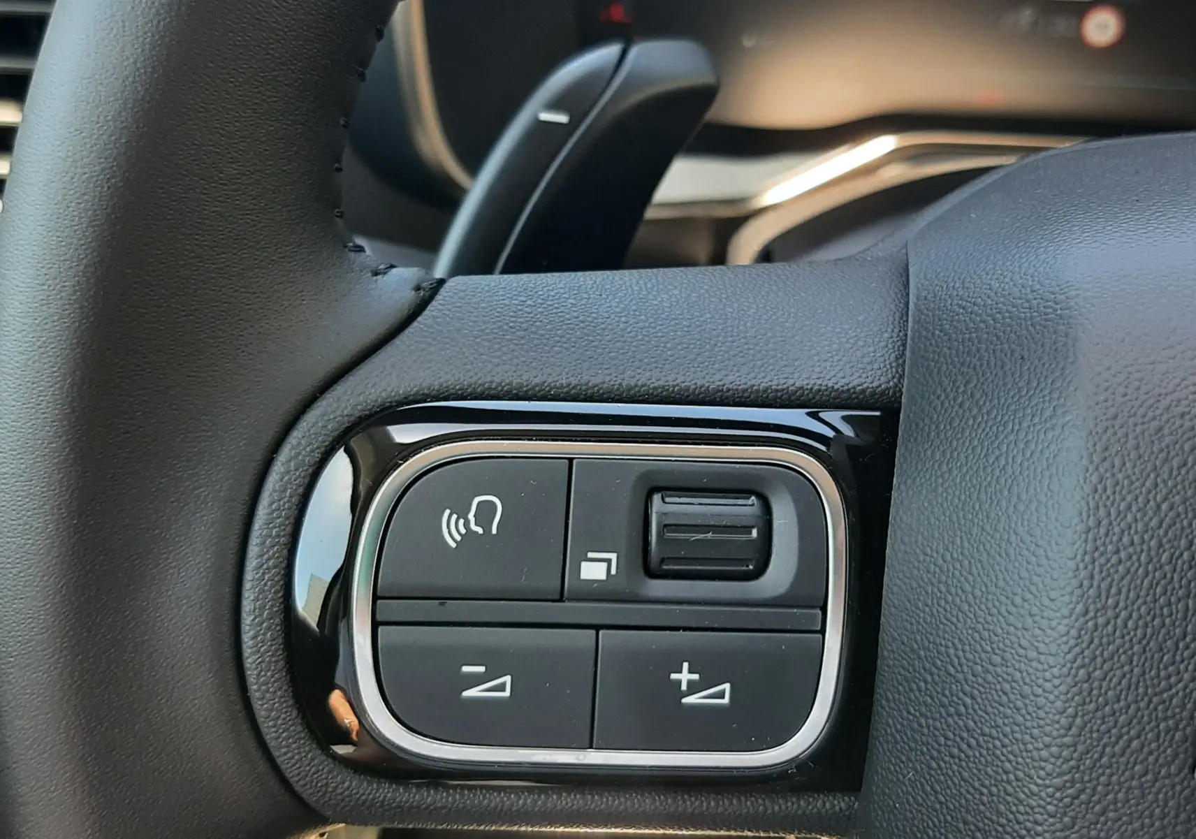 Gros plan sur les commandes gauche du volant noir du Citroën C5 Aircross hybride 2025, avec boutons de volume et interaction vocale.