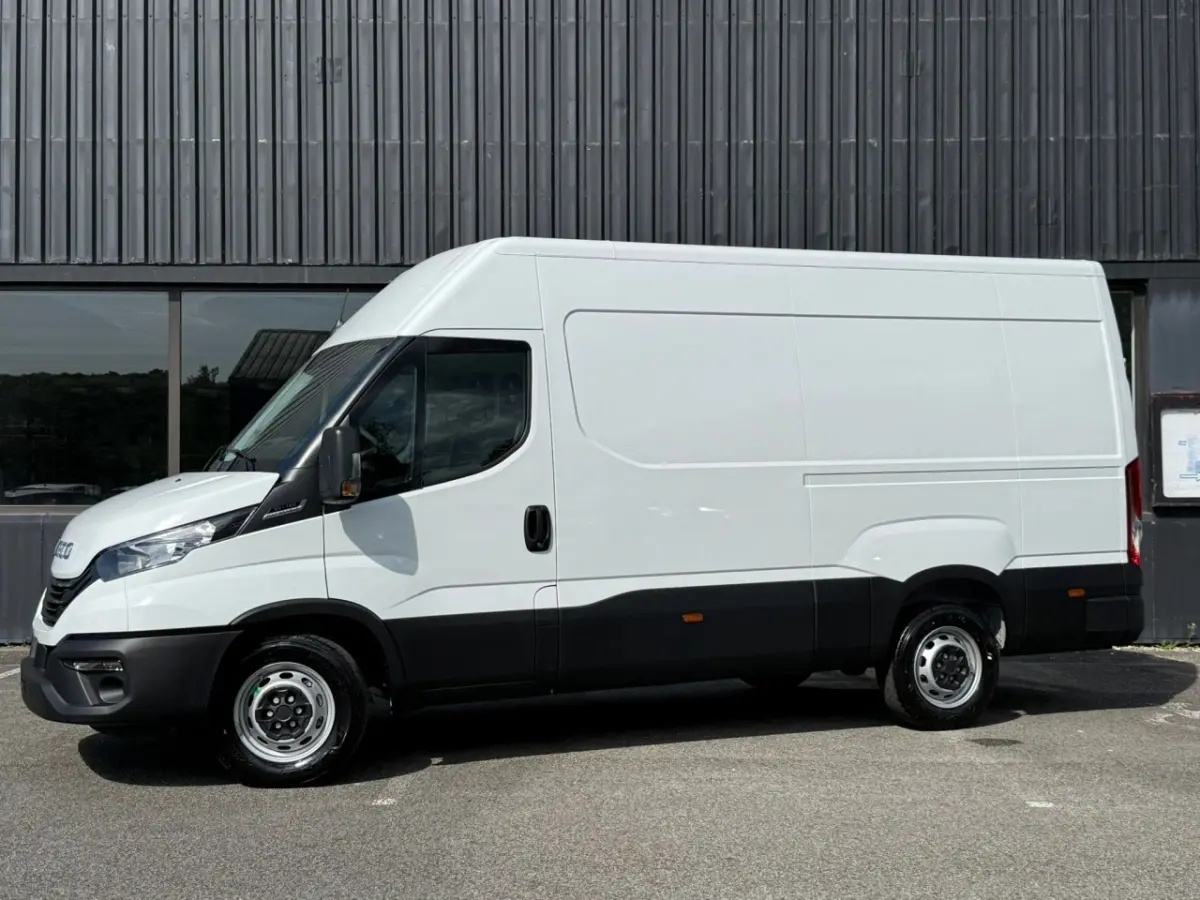 Vue de profil côté gauche d’un utilitaire Iveco Daily blanc avec bas de caisse noir, sans marquages, sur fond industriel.