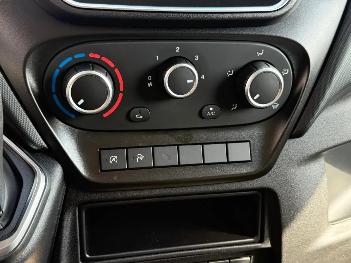 Gros plan sur les commandes de climatisation et boutons fonctionnels du tableau de bord noir de l'Iveco Daily 2.3 blanc.