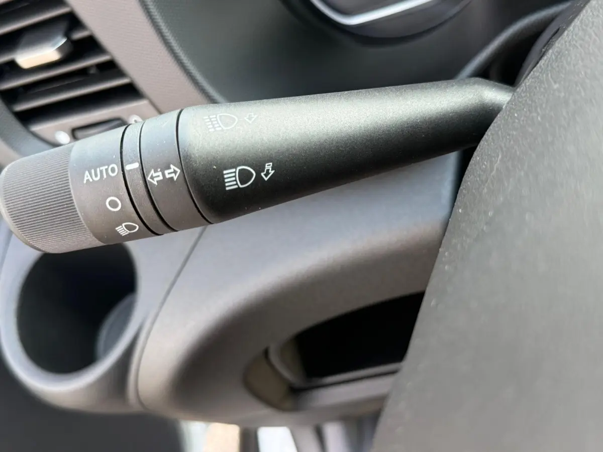 Gros plan sur la commande des phares et clignotants à gauche du volant dans l’habitacle gris de l’Iveco Daily blanc.