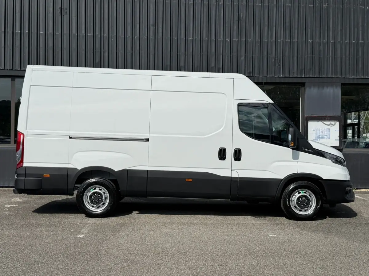 Fourgon Iveco Daily blanc vu de profil côté gauche, avec bas de caisse noir et porte coulissante latérale.