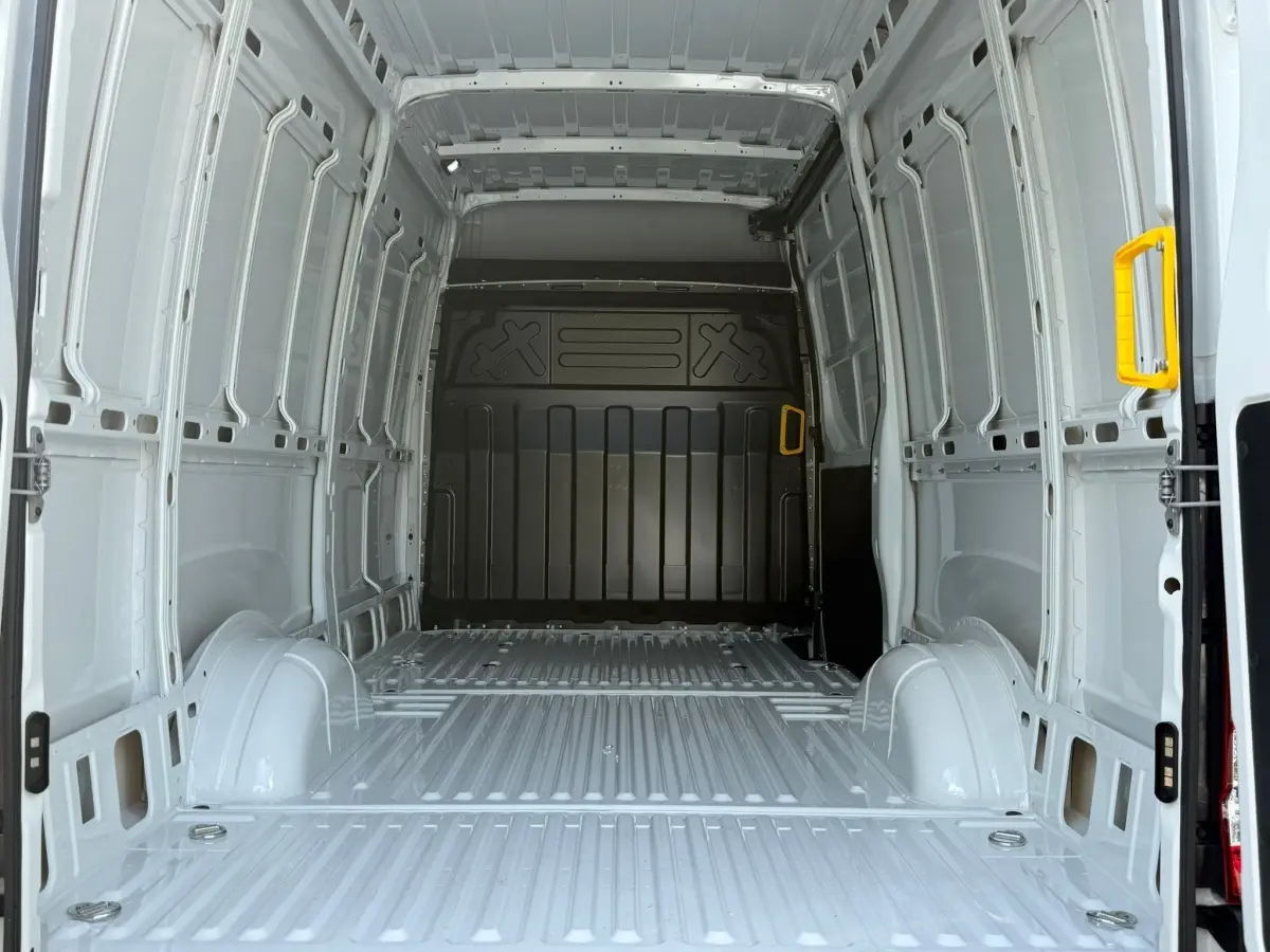 Vue intérieure arrière du fourgon Iveco Daily blanc 2026, montrant l'espace de chargement vide avec poignées jaunes.