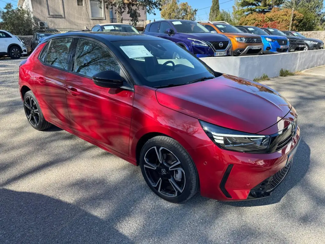 Opel Corsa rouge vue 3/4 avant droit, jantes noires et toit noir, stationnée en extérieur au soleil.