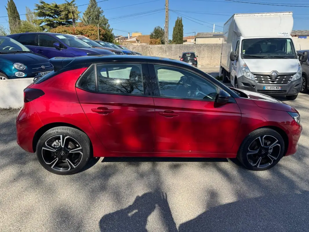 Vue de profil côté gauche d'une Opel Corsa rouge 2025 avec jantes noires et toit noir, garée en extérieur.