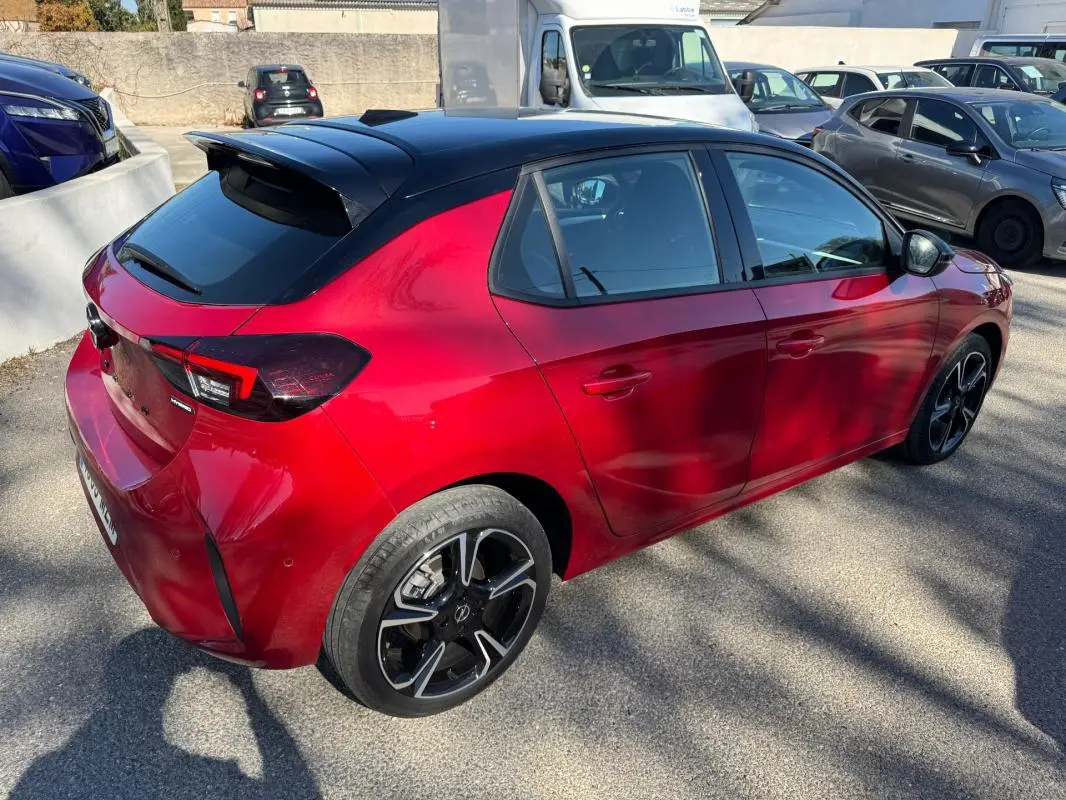 Vue 3/4 arrière droite d'une Opel Corsa rouge 2025 avec toit noir et jantes alliage noires distinctives.