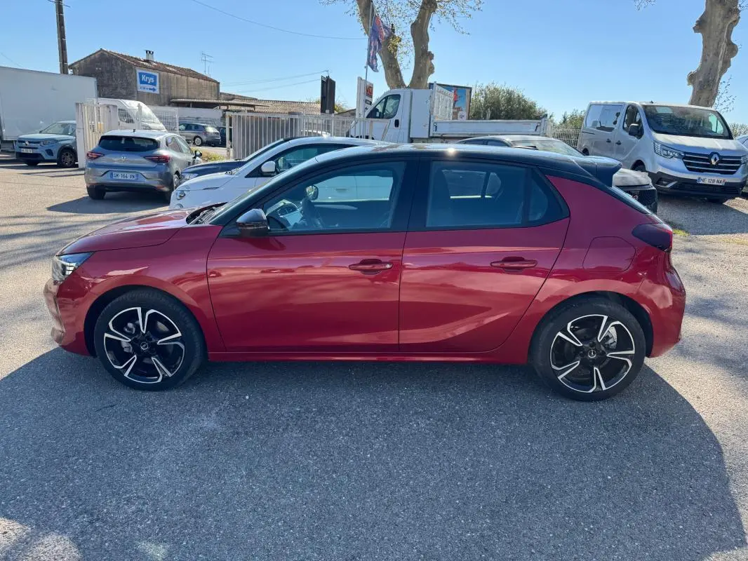 Vue latérale côté gauche d'une Opel Corsa 1.2 Turbo Hybrid rouge 2025 avec toit noir et jantes noires à motifs argentés.