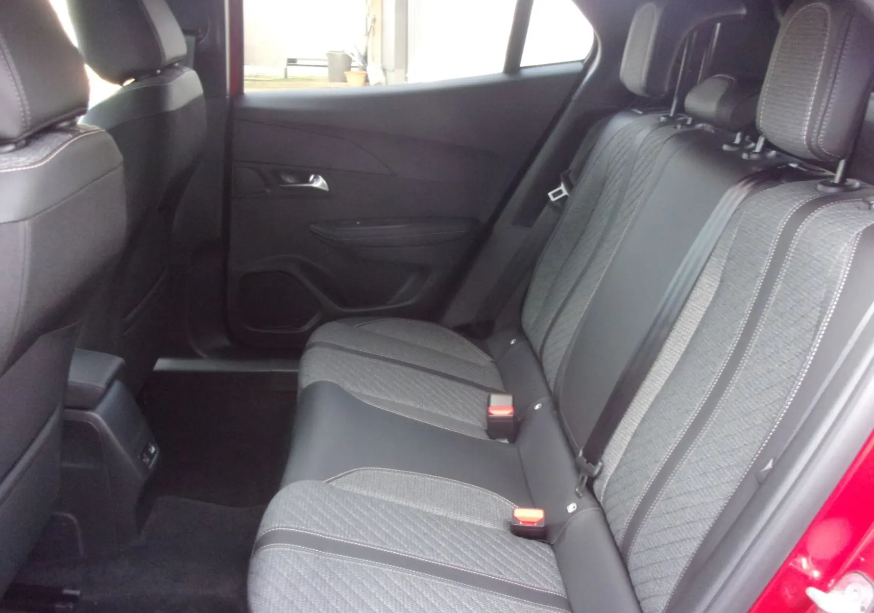 Vue intérieure arrière droite des sièges arrière gris texturés du Peugeot 2008 Rouge Elixir 2024 avec ceinture de sécurité visible.