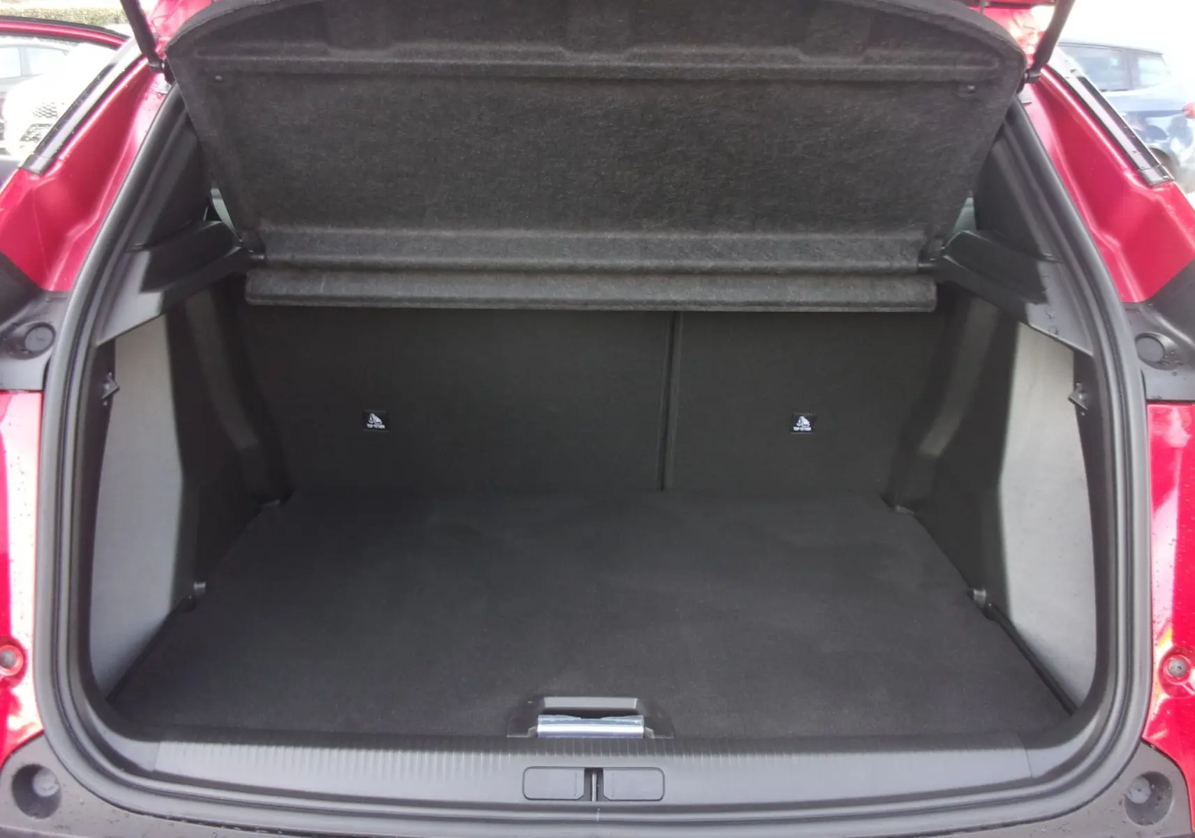 Coffre ouvert vu de l'arrière d'un Peugeot 2008 rouge Elixir, montrant un espace de chargement vide et propre.