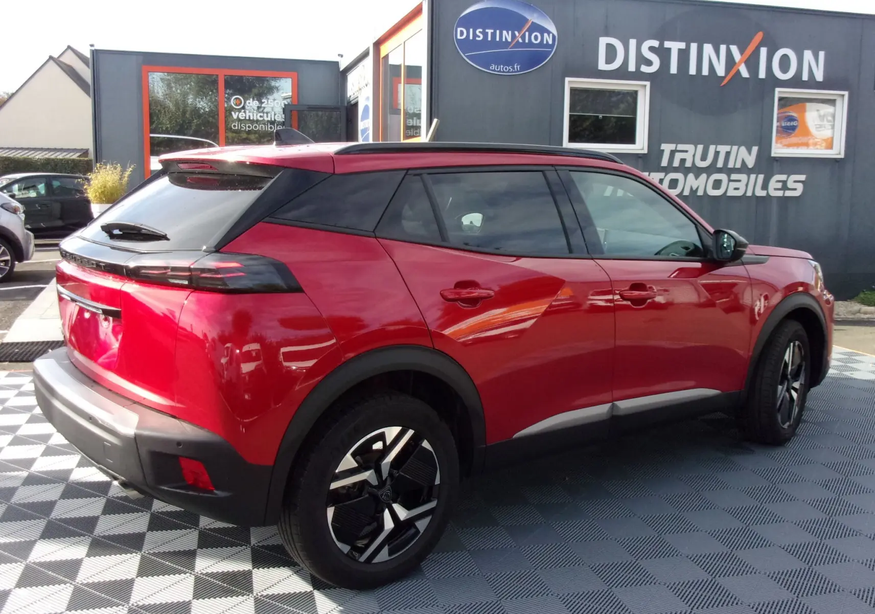 Vue 3/4 arrière droite d'un Peugeot 2008 2024 rouge Elixir avec toit noir et jantes alliage modernes.