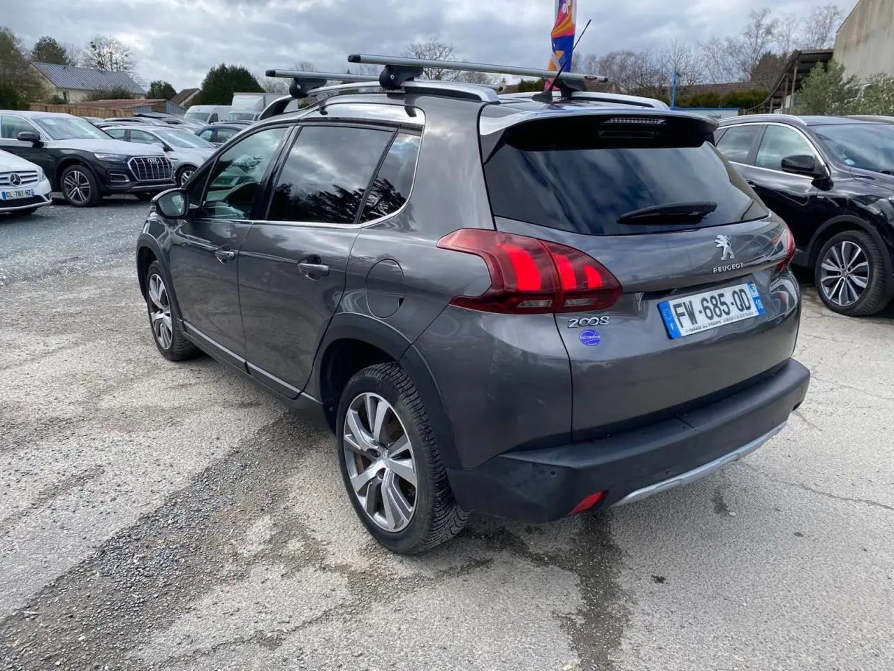Peugeot 2008 gris platinium vue 3/4 arrière droit avec barres de toit aluminium et vitres teintées.
