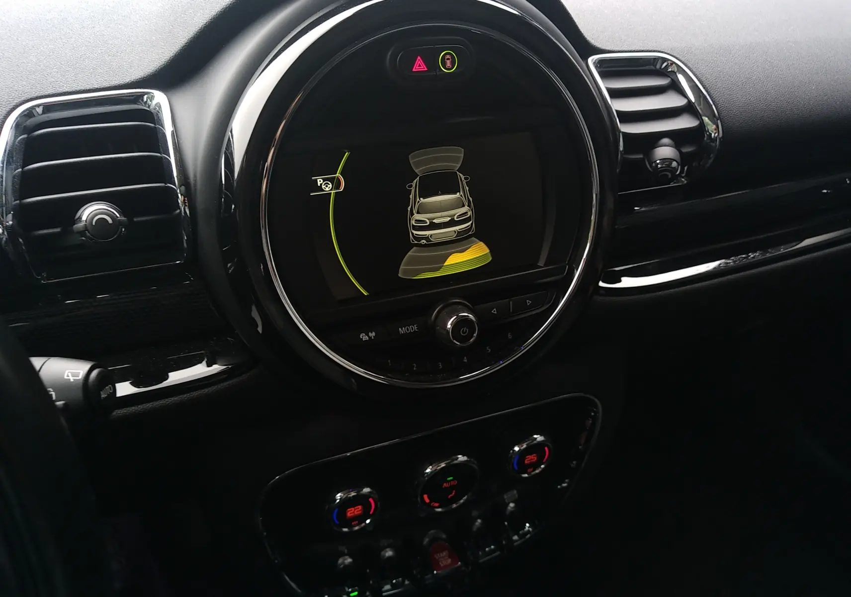 Vue intérieure du tableau de bord de la MINI CLUBMAN F54 avec écran central affichant l'aide au stationnement et commandes de climatisation.