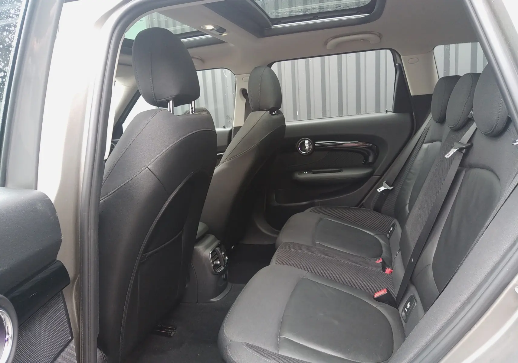 Vue intérieure arrière droite de la MINI CLUBMAN F54 2017, sièges noirs en cuir et tissu, toit ouvrant panoramique visible.