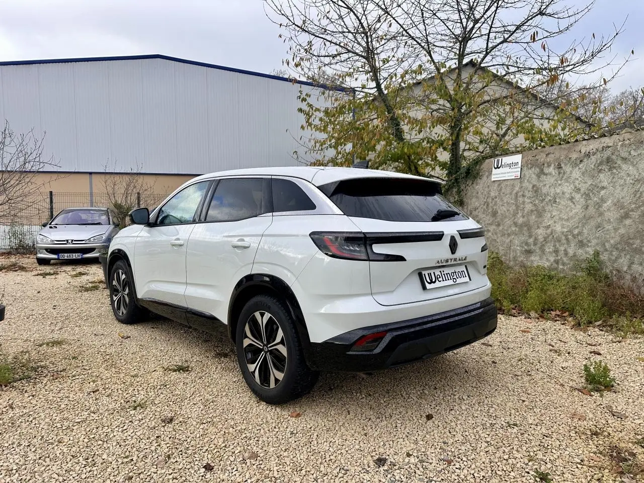 Renault Austral blanc vu en 3/4 arrière droit, avec feux arrière LED et vitres teintées sur terrain gravillonné.