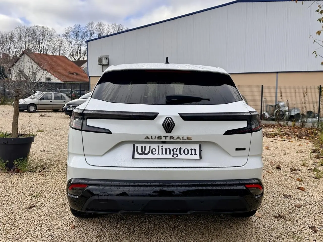 Vue arrière d'un Renault Austral blanc avec feux arrière étirés et logo central sur fond urbain.