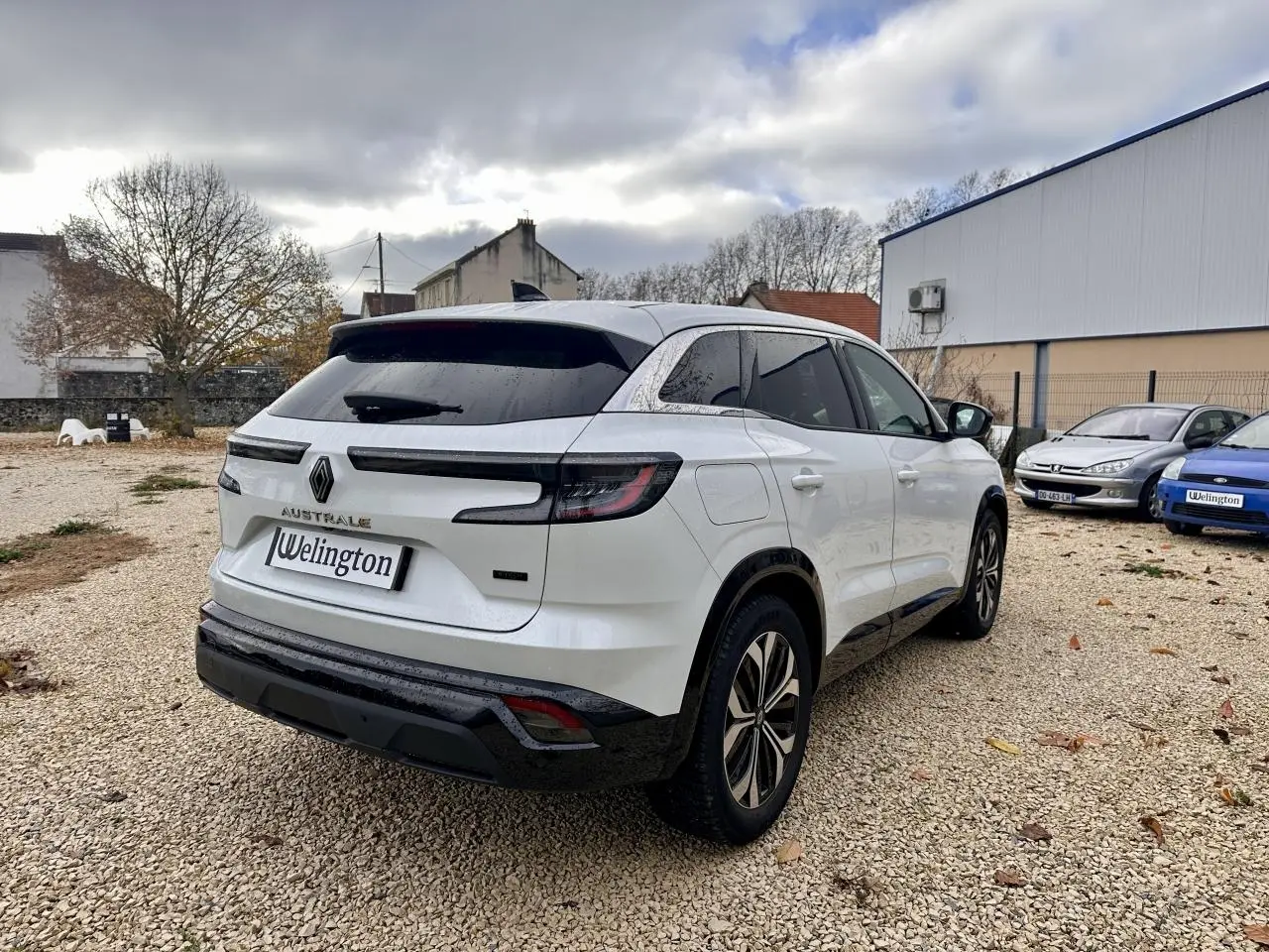 Renault Austral blanc en 3/4 arrière droit, avec feux LED et toit noir sur un parking extérieur.