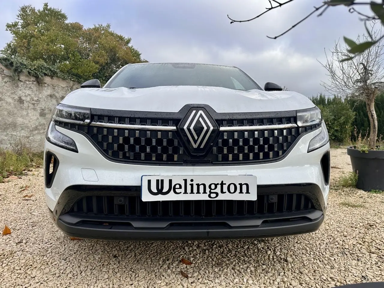Vue frontale rapprochée d'un Renault Austral blanc avec calandre noire à motif géométrique et logo central proéminent.