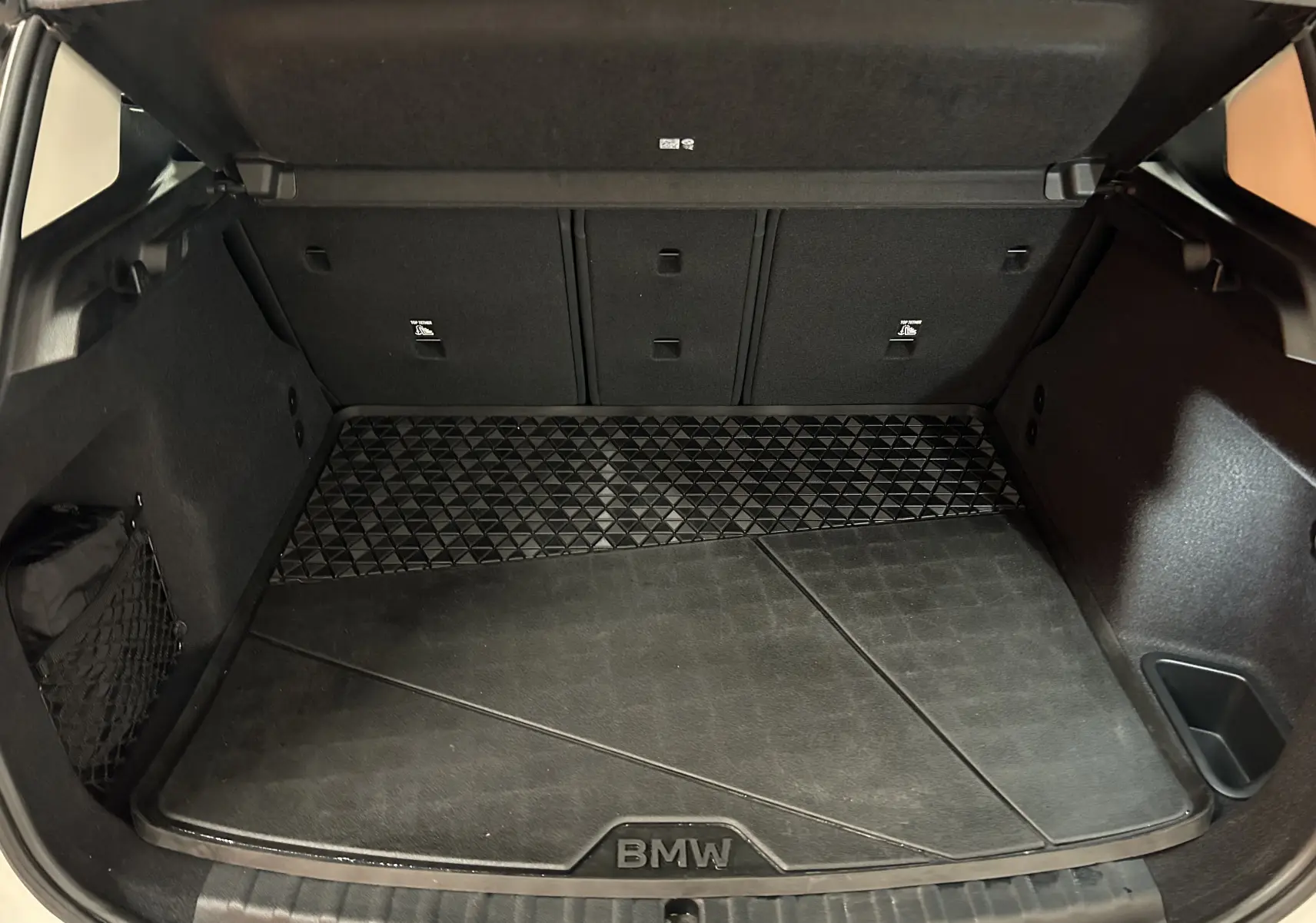 Vue du coffre ouvert de la BMW Série 2 Active Tourer blanc, montrant un tapis de coffre noir avec logo BMW.