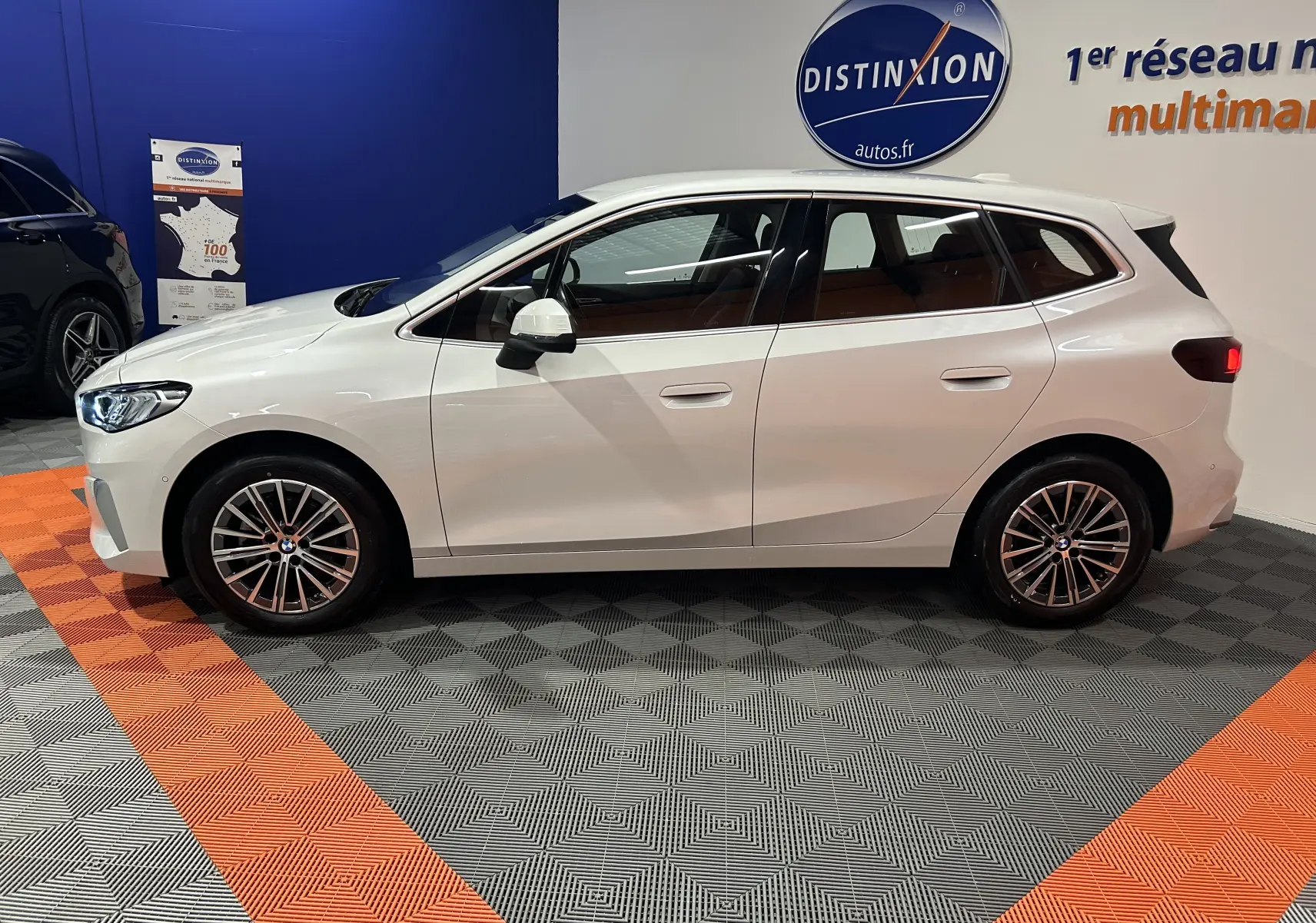 Profil droit d'une BMW Série 2 Active Tourer blanche 2022 avec jantes alliage et feux arrière allumés en showroom.