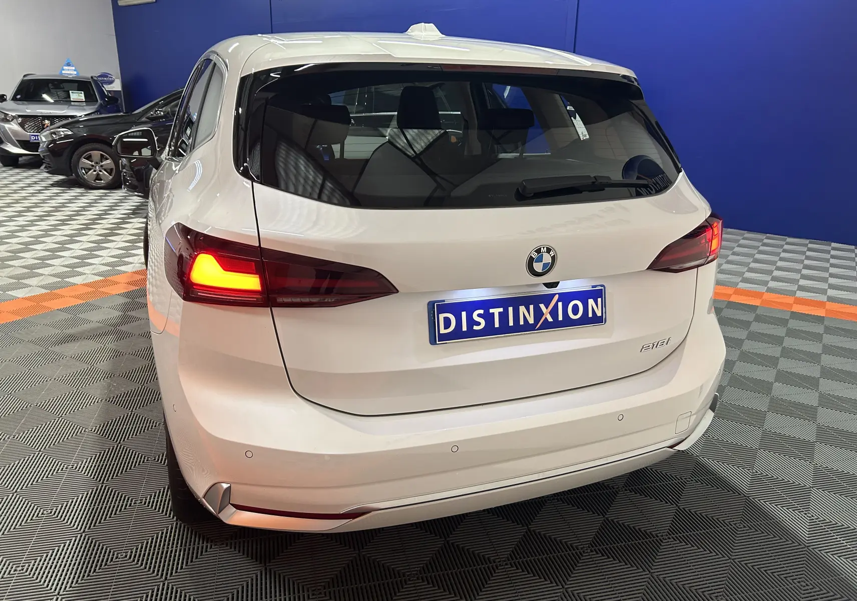 Vue 3/4 arrière d'une BMW Série 2 Active Tourer blanche avec feux arrière allumés dans un showroom.