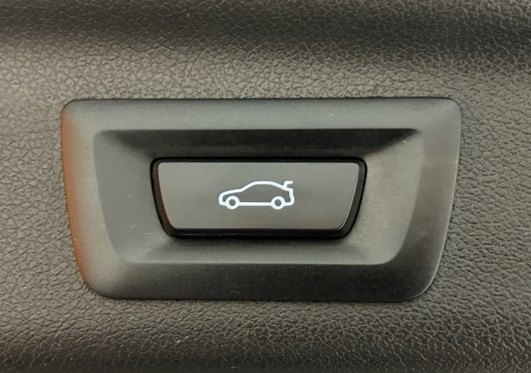 Gros plan sur le bouton noir d'ouverture électrique du hayon avec pictogramme blanc, intérieur d'un BMW Série 2 Active Tourer blanc.