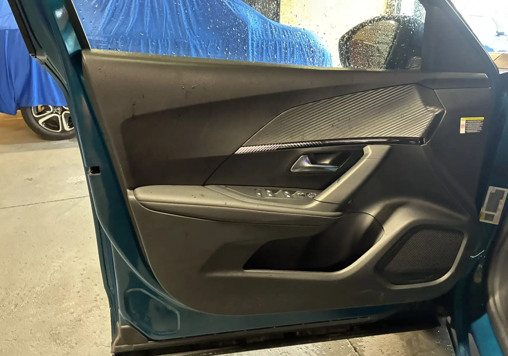 Vue intérieure de la porte côté gauche d’un Peugeot 2008 bleu 2025, avec garniture noire et insert effet carbone.