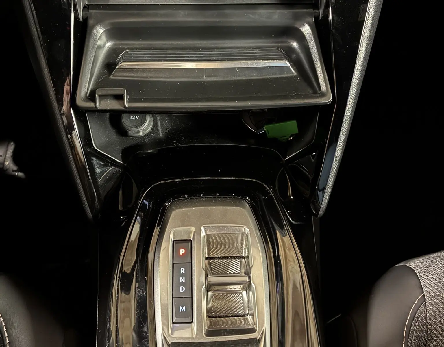 Vue plongeante sur la console centrale noire du Peugeot 2008 Hybrid 2025 avec levier de vitesses automatique et rangement ouvert.