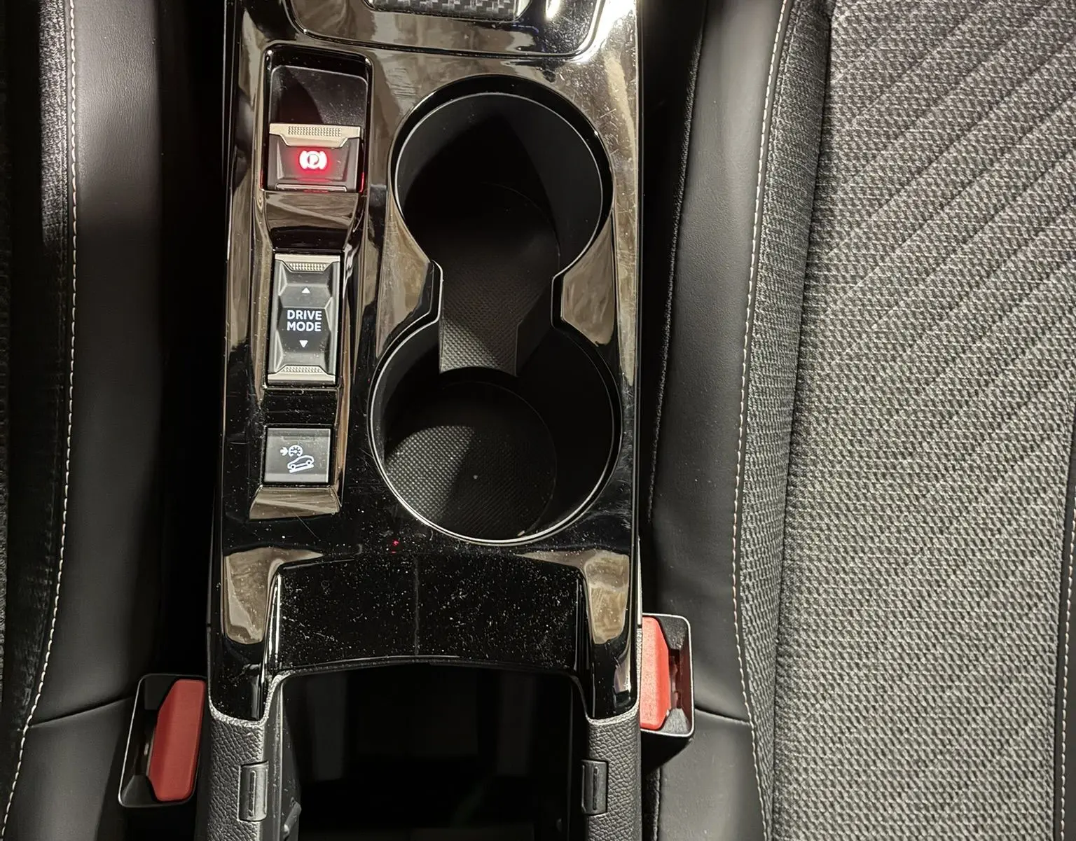 Vue plongeante sur la console centrale noire brillante du Peugeot 2008 1.2 Hybrid 136, avec porte-gobelets et commandes.