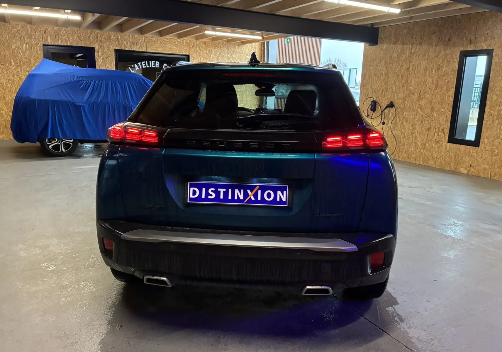 Vue arrière d’un Peugeot 2008 bleu 2025 hybride avec feux LED allumés dans un garage éclairé.