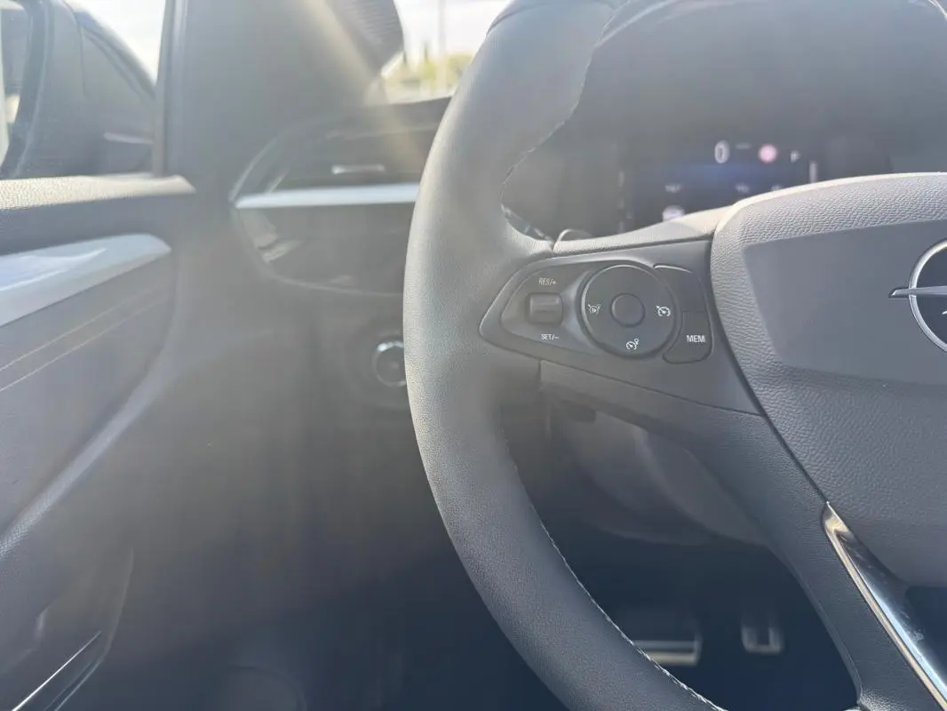 Gros plan sur le volant côté gauche de l’Opel Corsa noir 2025, avec commandes intégrées et tableau de bord en arrière-plan flou.