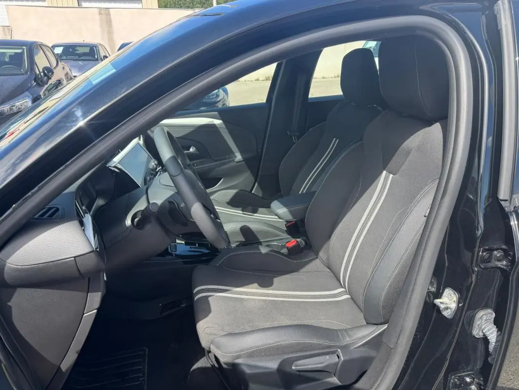 Vue intérieure côté conducteur de l’Opel Corsa 2025 noire, montrant les sièges tissu avec bandes claires et le tableau de bord moderne.