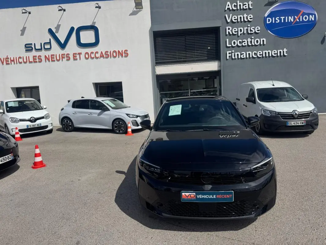 Opel Corsa 1.2 Turbo Hybrid noir vue de face, stationnée devant un concessionnaire avec d'autres véhicules autour.