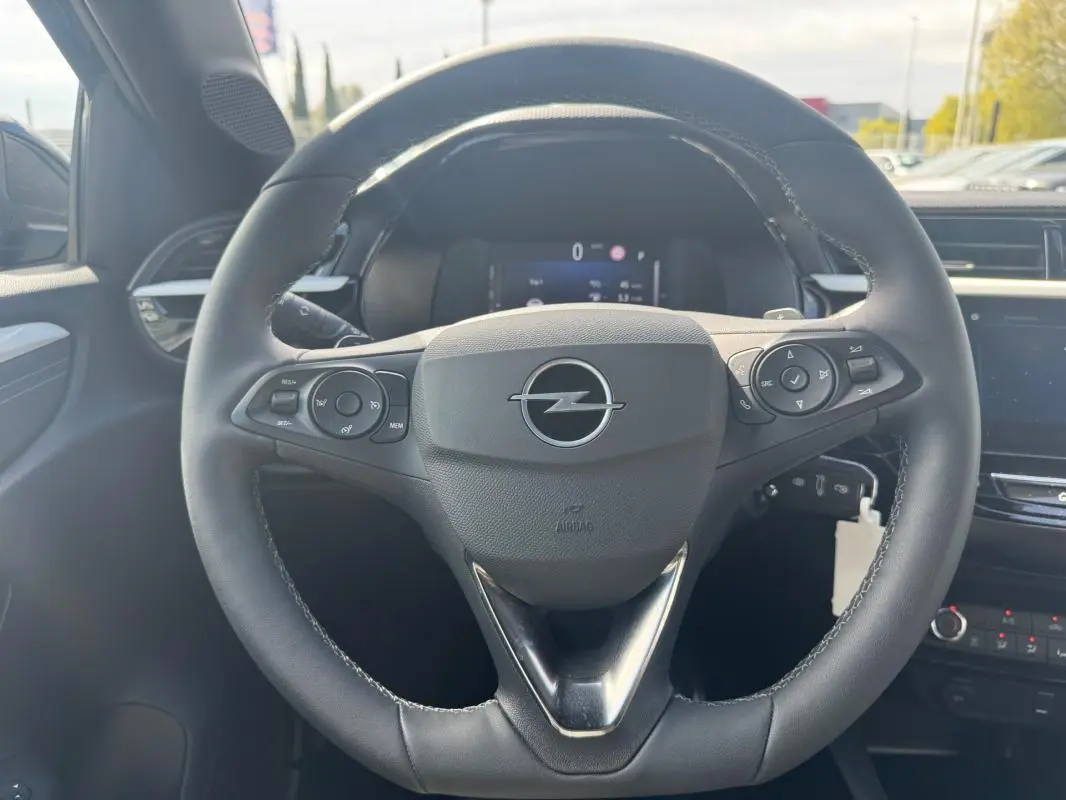 Vue rapprochée du volant noir de l’Opel Corsa 2025 avec commandes intégrées et tableau de bord numérique en arrière-plan.