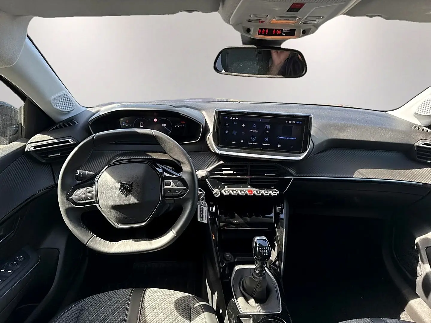 Vue intérieure avant de la Peugeot 208 1.2 100 Allure 2025, tableau de bord noir avec écran tactile et volant compact.
