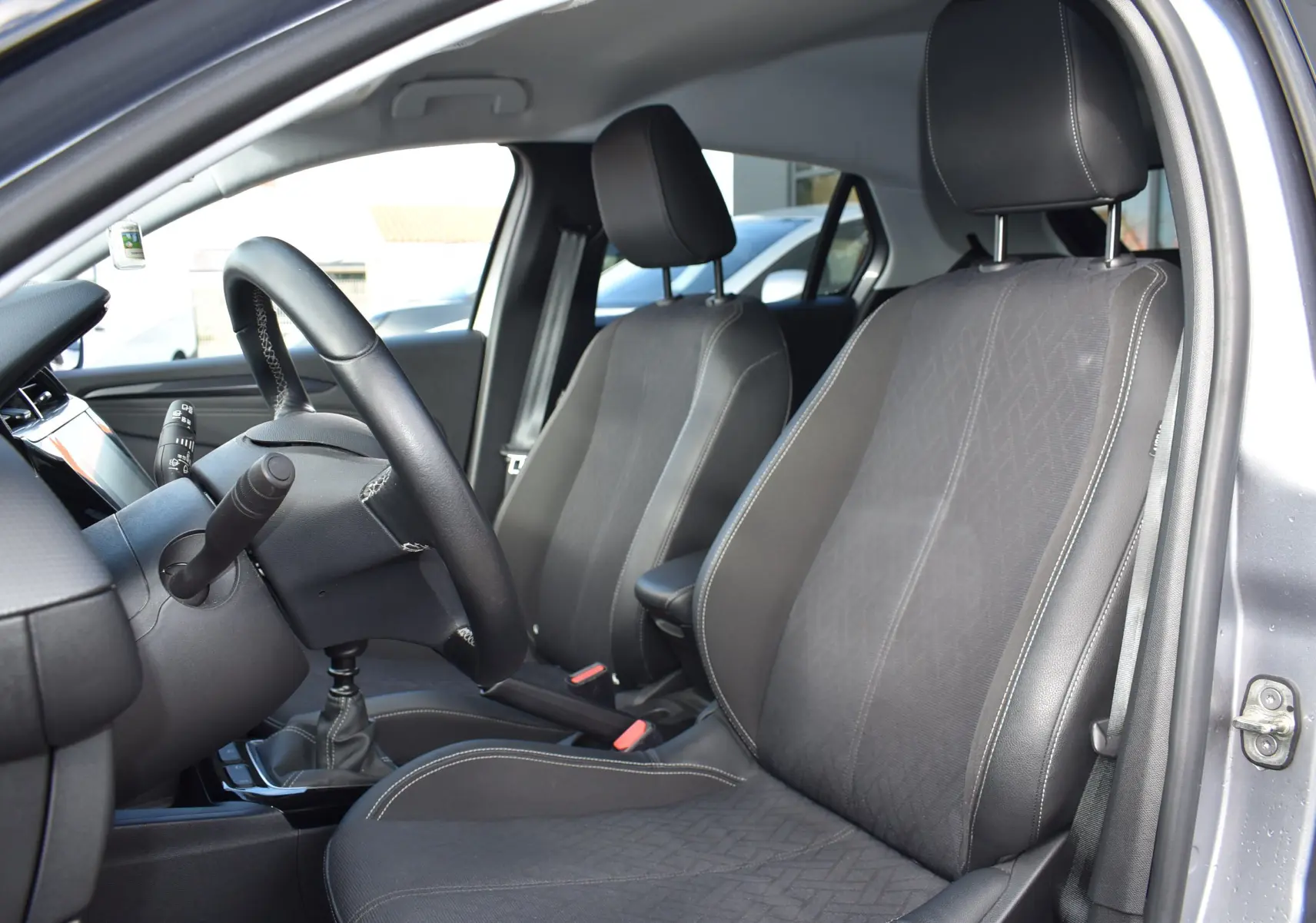 Intérieur avant droit de l'Opel Corsa gris 2021, sièges tissu noir avec surpiqûres blanches et volant cuir.