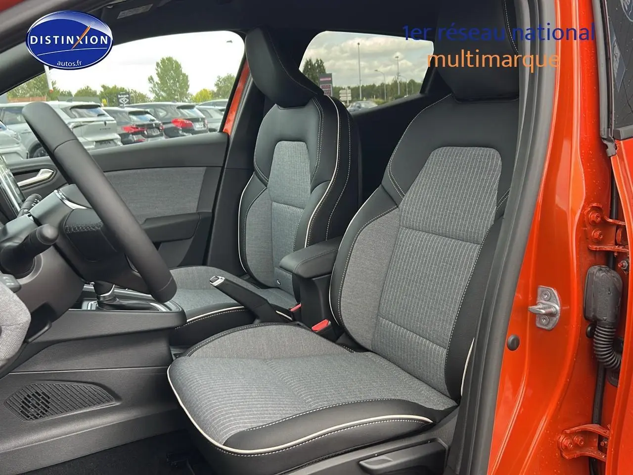 Intérieur de la Renault Clio V orange Valencia, vue côté droit sur les sièges avant sport gris avec surpiqûres blanches.