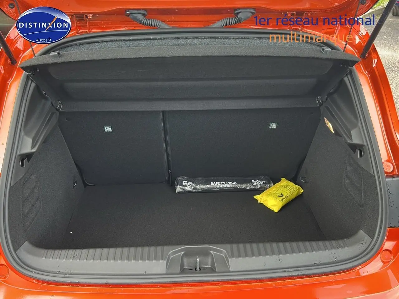 Coffre ouvert d'une Renault Clio V orange Valencia, montrant un espace de rangement avec kit de sécurité noir et jaune.