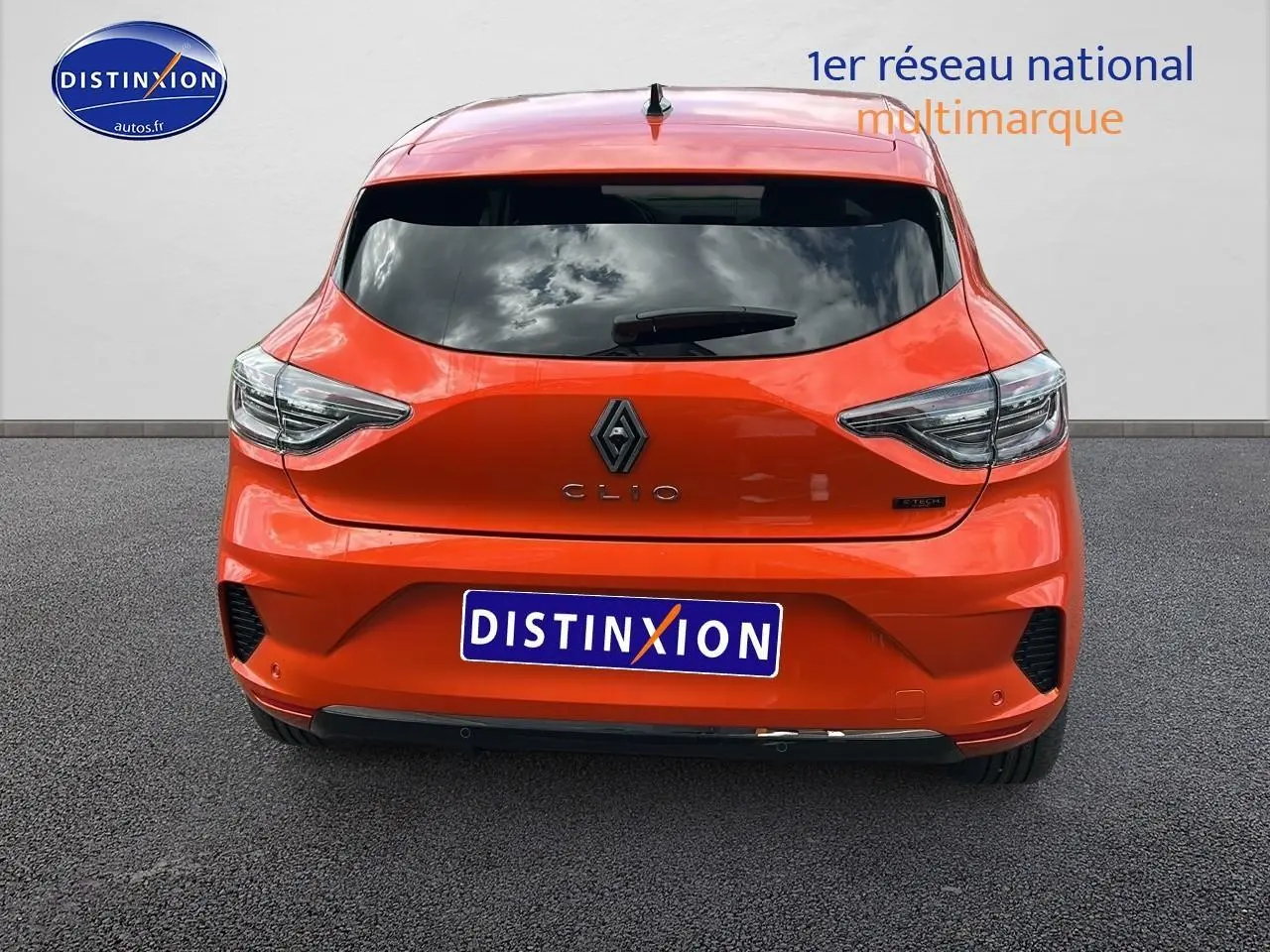 Vue arrière d'une Renault Clio V orange Valencia avec feux LED et logo central sur fond urbain gris.