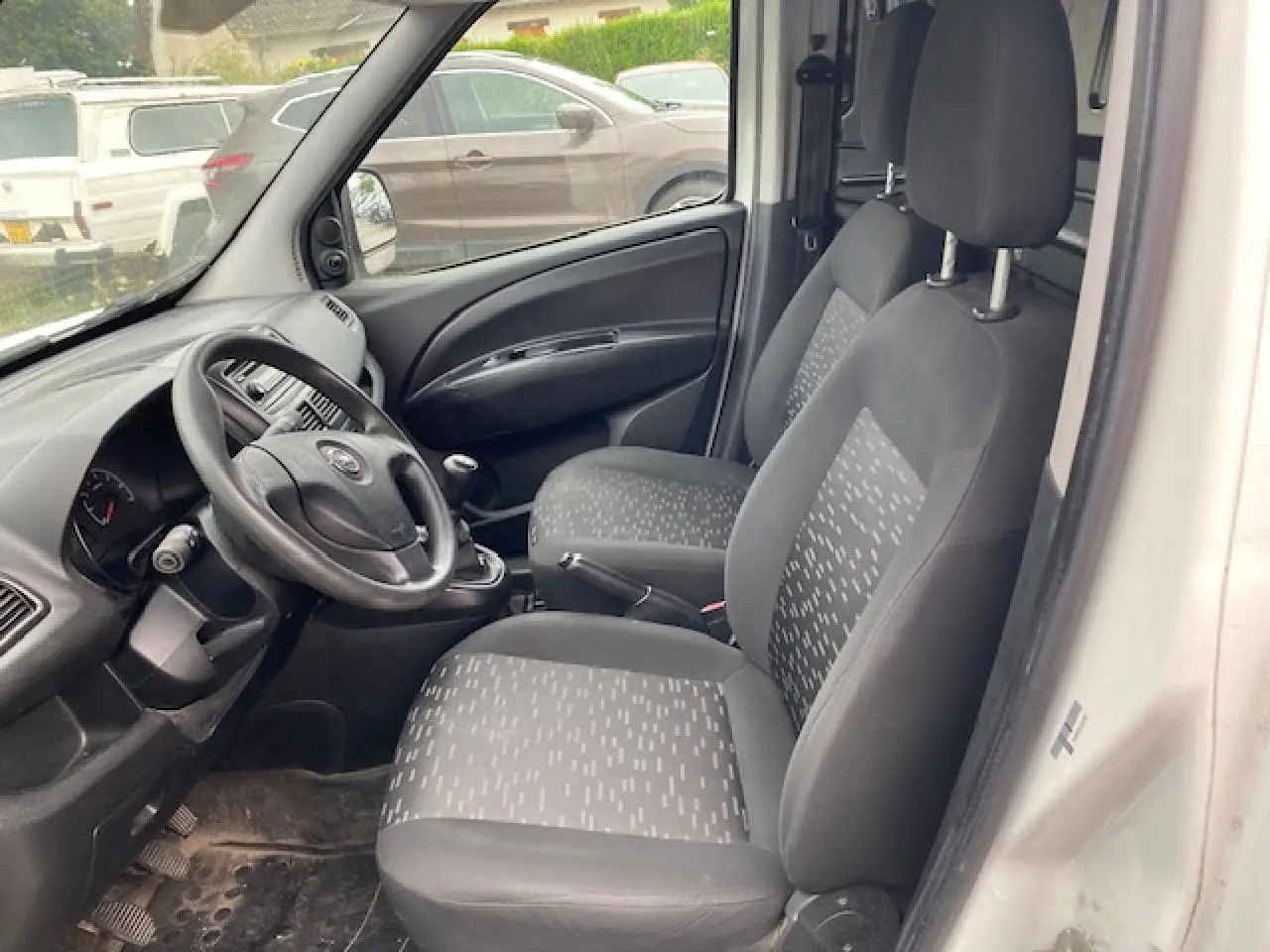 Vue intérieure côté conducteur de l'Opel Combo blanc 2016, montrant sièges tissu gris et tableau de bord simple.