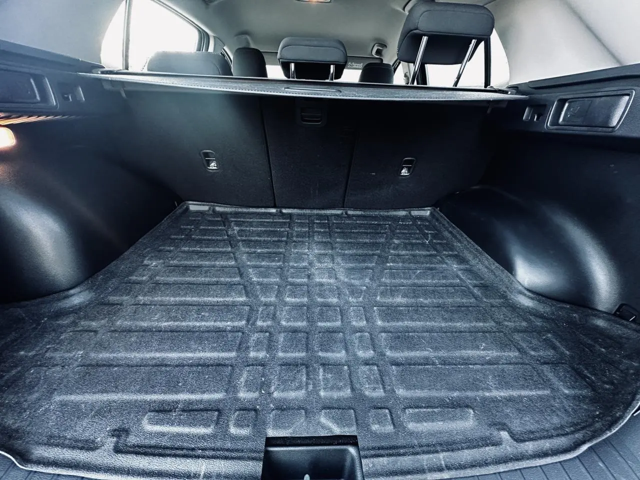 Vue intérieure du coffre noir du Kia Sportage 2023 avec banquette arrière et cache-bagages visibles.