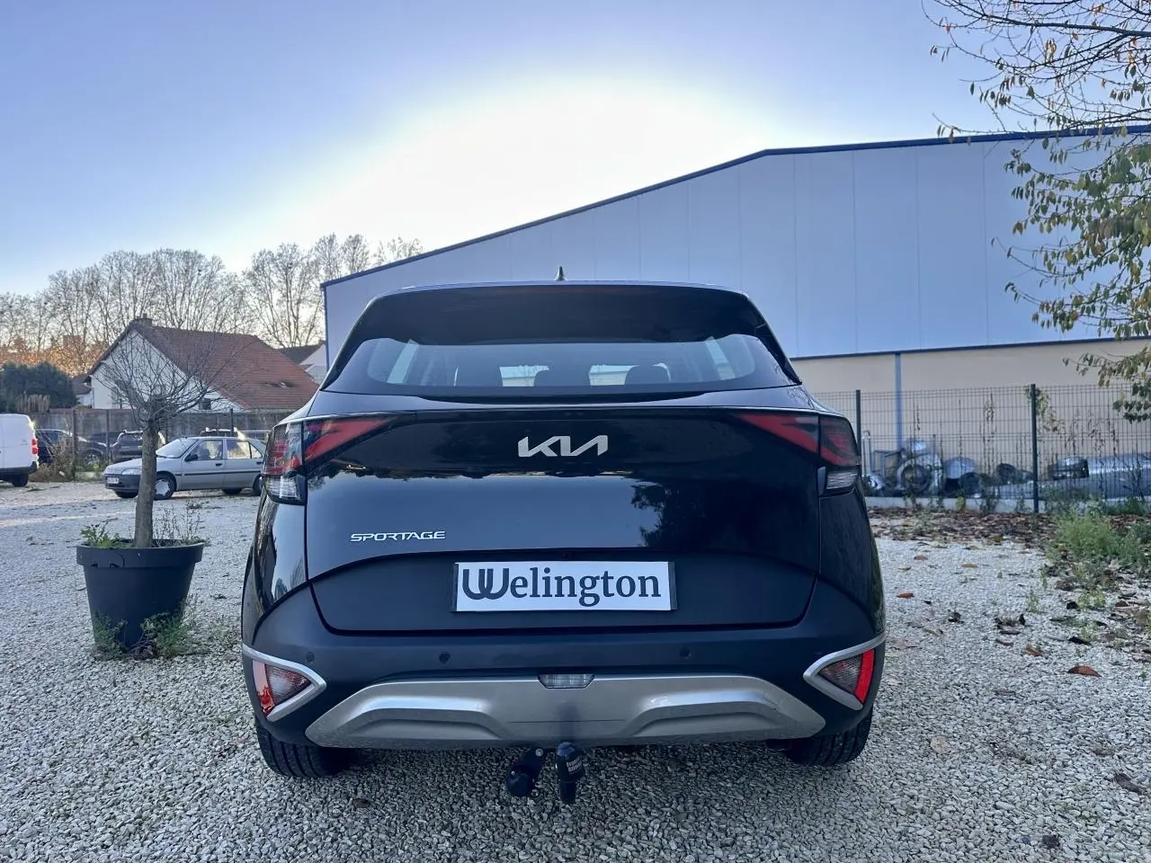 Vue arrière d'un Kia Sportage noir 2023 avec attelage et feux arrière LED distinctifs sur un sol gravillonné.