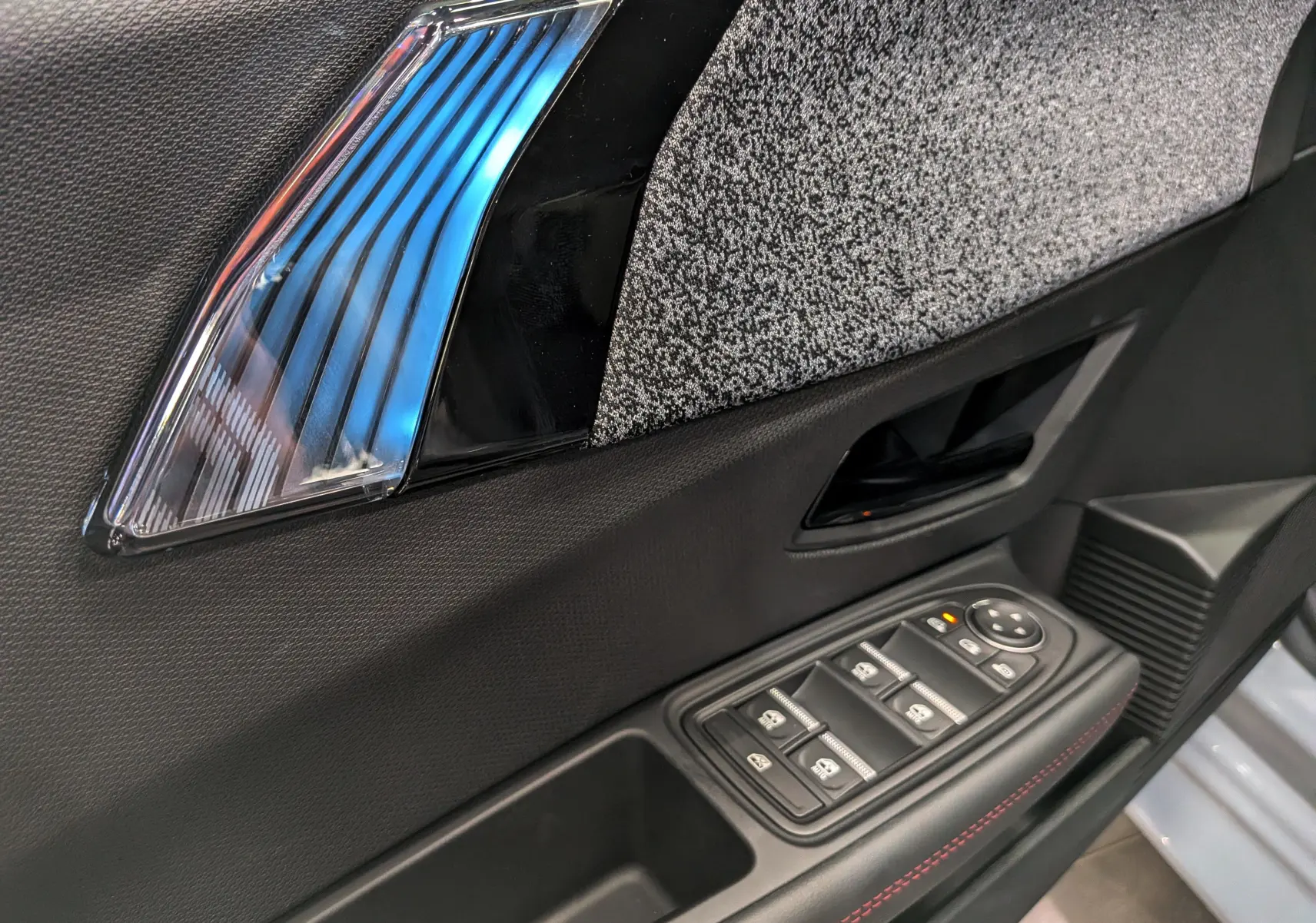 Détail de la porte côté conducteur de la Renault Clio VI TCe 115 Gris Rafale, avec commandes de vitres et insert décoratif bleu.