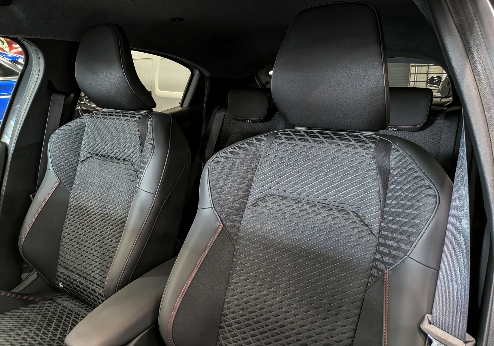 Vue rapprochée des sièges avant en tissu noir et cuir avec surpiqûres rouges dans une Renault Clio VI TCe 115 Gris Rafale.