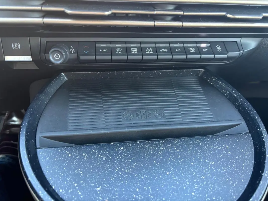Vue rapprochée de la console centrale de la Lancia Ypsilon 2025 avec commandes climatisation et surface de recharge sans fil noire à motifs gris.
