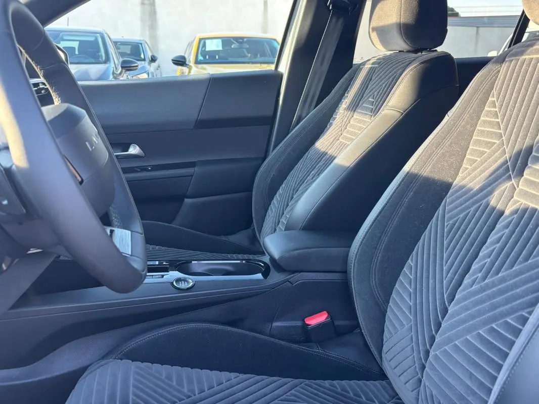 Vue intérieure côté conducteur de la Lancia Ypsilon 2025, sièges en tissu gris avec motifs géométriques et volant sport.