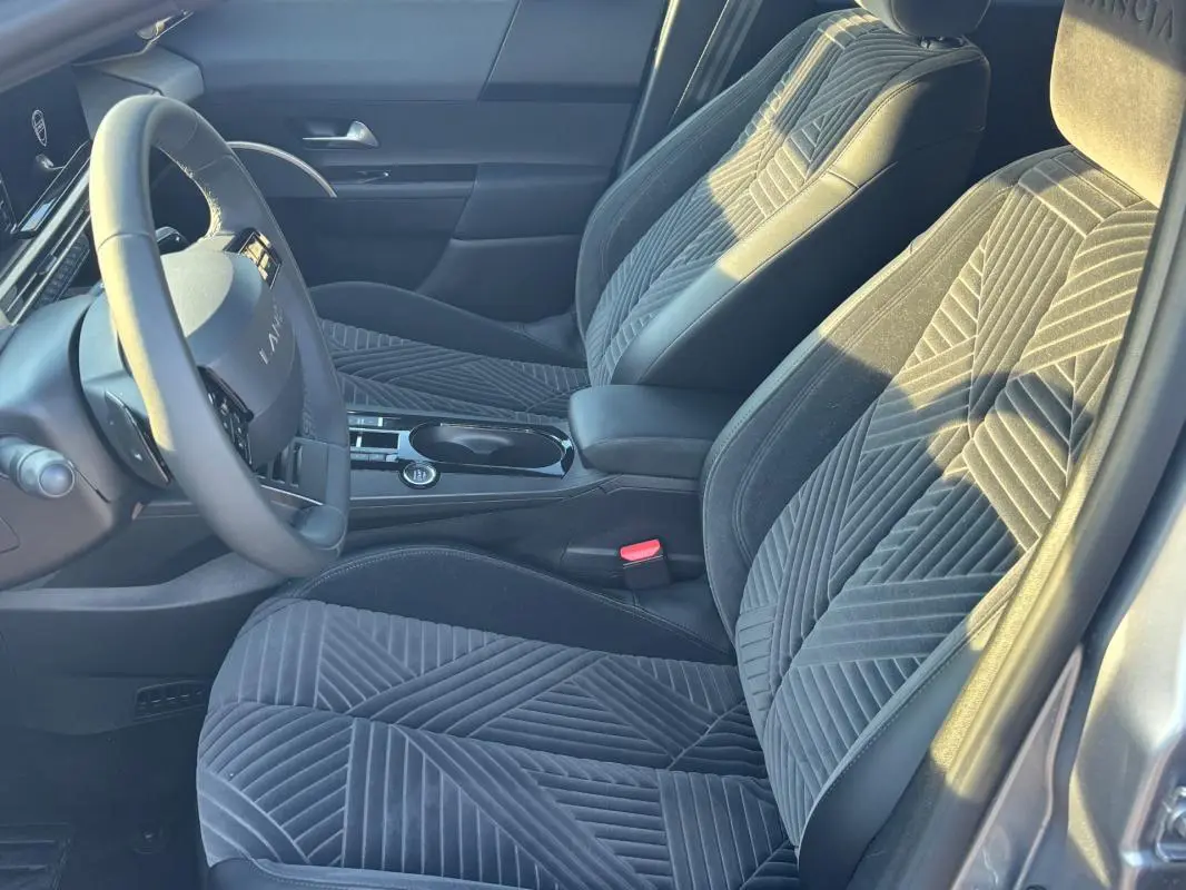 Vue intérieure côté conducteur de la Lancia Ypsilon gris 2025, mettant en valeur les sièges en tissu à motifs géométriques et le volant sport.