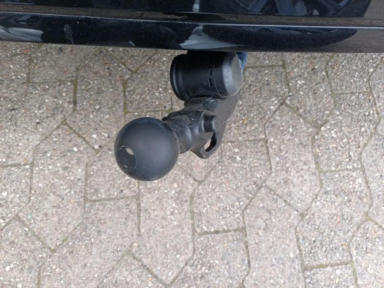 Gros plan sur l'attelage escamotable noir sous le pare-chocs arrière d'une Volkswagen Golf noire métallisée.