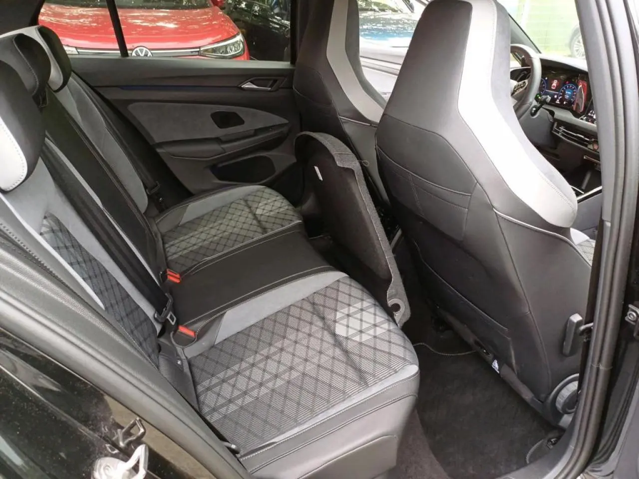 Vue intérieure côté arrière gauche de la Volkswagen Golf noire avec sièges arrière en tissu à motif losanges et cuir noir.